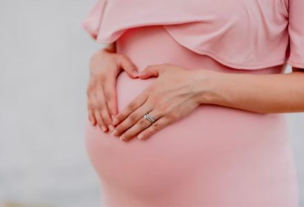 A picture of a pregnant woman in a pink dress holding her stomach