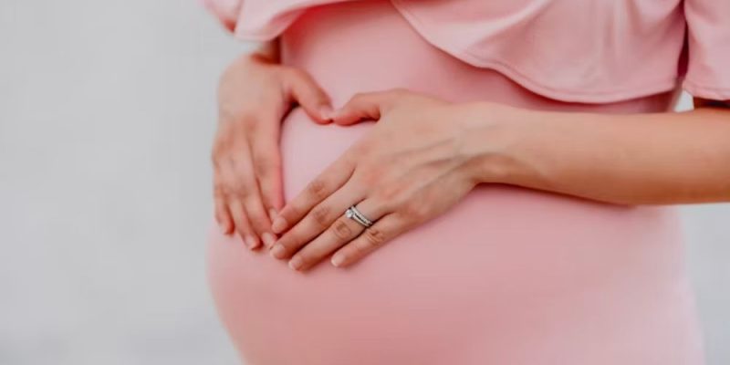 A picture of a pregnant woman in a pink dress holding her stomach